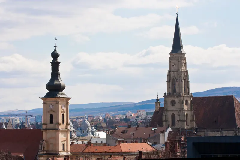 Acoperișurile centrului Clujului cu turla Bisericii Sfântul Mihail și dealurile în fundal