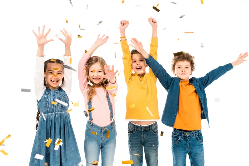 Patru copii veseli cu mâinile ridicate, sub o ploaie de confetti