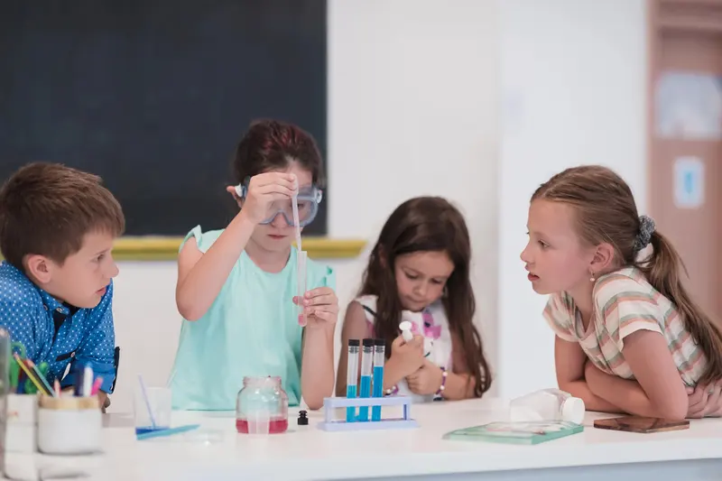 Copil cu ochelari de protecție turnând lichid într-o eprubetă, la un atelier de științe