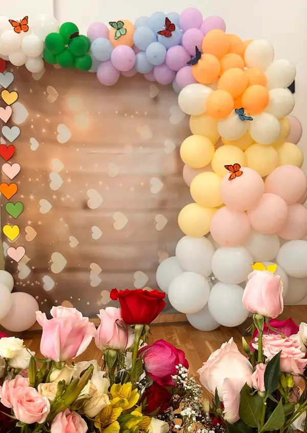 Decor de serbare cu arcadă de baloane colorate și buchete de flori.