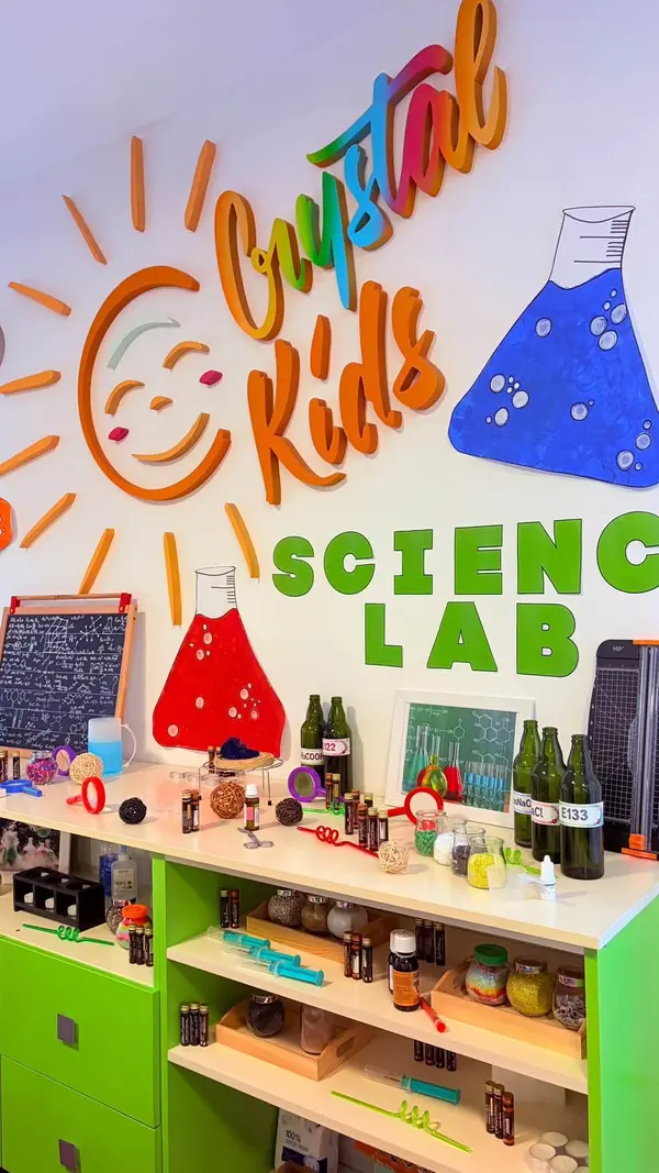 Colțul Science Lab cu logo Crystal Kids pe perete și rafturi verzi pline cu materiale de experimente.
